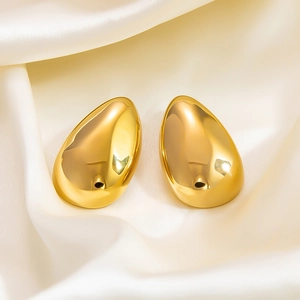 Detailed close-up of gold hollow teardrop earrings on white elegant satin fabric