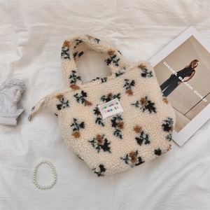 Detail einer floralen Sherpa-Handtasche mit Markenlabel auf weißem Stoffhintergrund