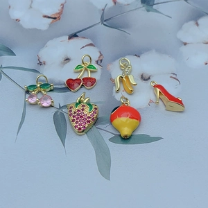 Macro shot of fruit charms like cherry and strawberry in gold metal with enamel detail