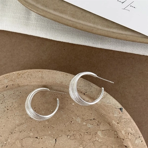 Elegant multi-layered silver C-shaped stud earrings on a ceramic display tray