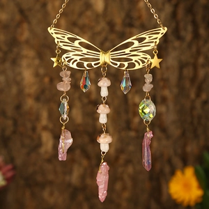 Detail of golden butterfly suncatcher with pink crystals and ceramic mushrooms hanging outdoors