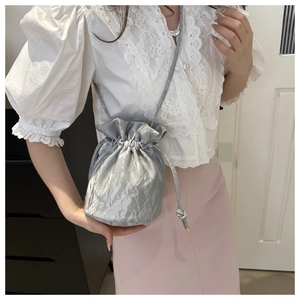 Silver drawstring bucket bag with metallic crinkled texture shown on shoulder