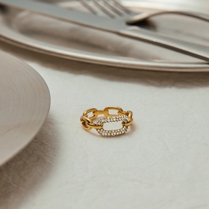 Elegante anello a catena dorata con zirconi incastonati su sfondo in tessuto grigio