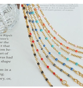 Detailed view of multiple gold necklaces with colorful enamel beads on vintage book pages