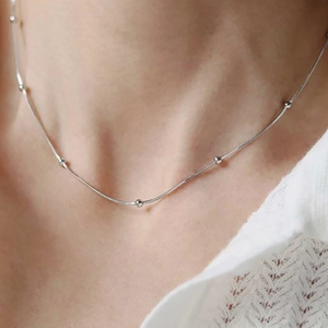 Detail view of a silver snake chain necklace with beads worn on the neck