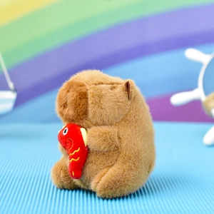 Adorable brown plush Capybara keychain pendant holding a red fish on textured blue surface