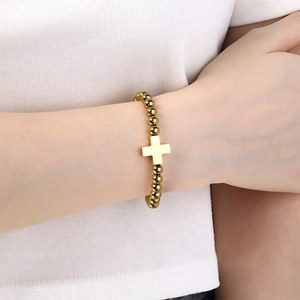 Detail of a minimalist gold cross bead bracelet on a female model with polished finish