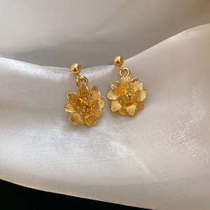 Detailed close-up of golden flower drop earrings with textured petals on white satin fabric