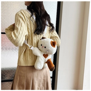 Detail shot of a plush calico cat crossbody bag worn over a beige sweater and skirt