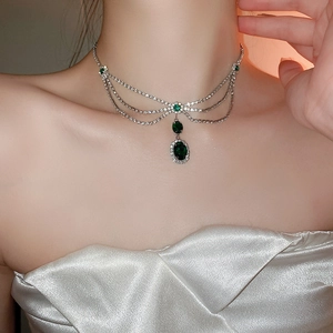 Close-up of elegant layered silver necklace with emerald green crystals on a model