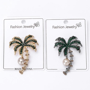 Detailed view of gold and black palm tree brooches with green rhinestones and pearls