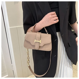 Detail of beige square handbag with gold H buckle on black blazer and white skirt