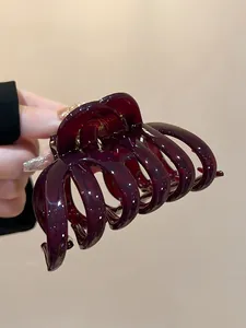 Detail view of a large burgundy acrylic shark hair claw with strong golden metal spring