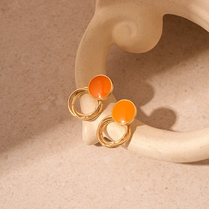 Detailed close-up of orange enamel and gold-plated circular stud earrings on beige stand