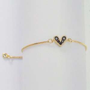 Elegant gold heart bracelet for women with black zircons on a white cylinder stand