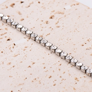 Square-cut silver tennis bracelet with sparkling zircons on a textured stone surface