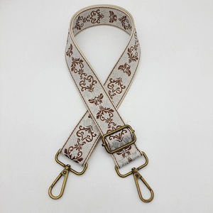 Close-up of wide embroidered beige and brown bag strap with adjustable metal buckle