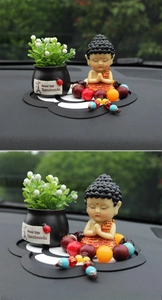Detail of praying monk car ornament with floral pot and beads on a non-slip petal mat