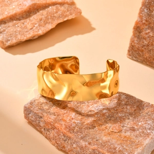 Detailed view of a wide textured gold metal bangle placed on a natural reddish stone