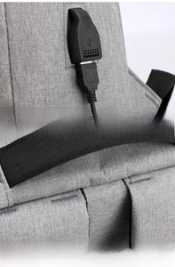 Detail of USB charging port and reinforced shoulder strap stitching on grey backpack