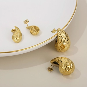 Close-up of golden teardrop earrings with hammered texture on white ceramic plate
