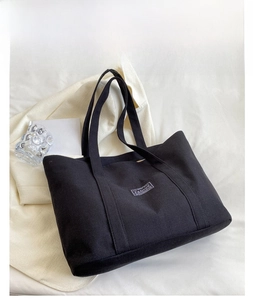 Detail shot of a black canvas tote bag with vintage patch on a white textured backdrop