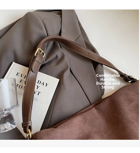Detailed close-up of brown suede tote bag with leather strap and golden metal buckle