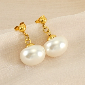 Detail of gold-plated earrings with large white baroque pearls on beige fabric