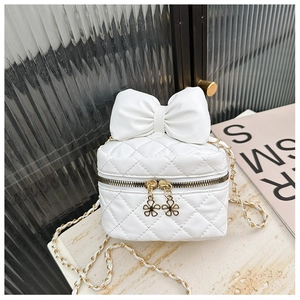 Detail of white quilted crossbody bag with decorative bow and gold flower zipper