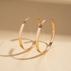 Detailed close-up of large flat gold hoop earrings with a mirror polished finish