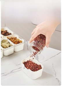 Action shot showing peppercorns poured into a multi-grid seasoning box on marble counter