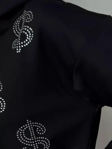 Macro detail of silver rhinestone dollar sign on black zip-up hoodie fabric