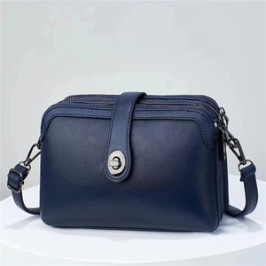 Deep blue leather crossbody bag with triple zippers and metallic swivel lock on white stand
