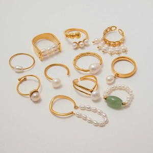 Flat lay of multiple pearl gold rings featuring chain links and oval gemstone accents