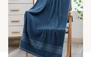 Close-up of deep blue cotton bath towel with gold stripes on a wooden chair