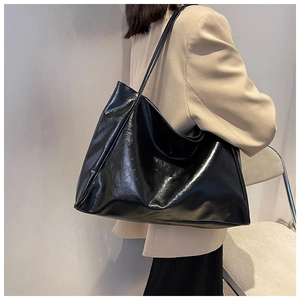 Glossy black large capacity tote bag worn on shoulder over a beige blazer jacket