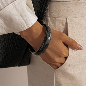 Close-up of a wide glossy black resin round bangle worn with a minimalist style outfit