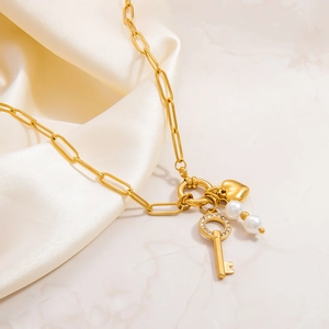Close-up of golden paperclip necklace with diamond key, heart pendant, and pearls