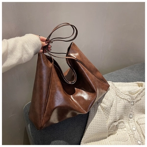Close-up of brown oiled leather tote bag being held by a model in a cozy indoor setting