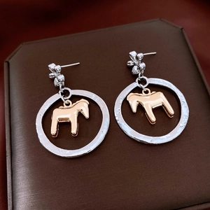 Detail of silver flower earrings with a golden horse pendant inside a metal ring