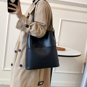 Modefrau im khakifarbenen Mantel mit großer schwarzer Leder-Eimertasche in der Hand