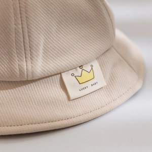 Detailed close-up of beige twill cotton kids bucket hat with Lucky Baby crown label