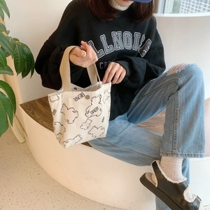 Detail of corduroy tote bag featuring bear prints and button closure held by a model