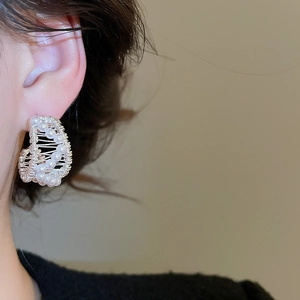 Macro detail of C-shaped 18k gold plated hoop earring with woven texture and white pearls