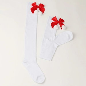 Detail of white over-knee Christmas socks featuring red satin bows and plush pom-poms