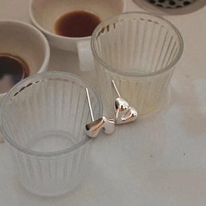 Close-up of minimalist 925 sterling silver heart-shaped stud earrings on a glass rim