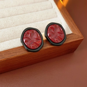Macro shot of irregular vintage earrings with black frames and lava-textured red resin inlay