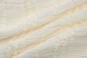 Vue macro de la texture plissée blanche et du motif tissé délicat de cette robe chic