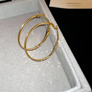 Macro detail of large gold hoop earrings with faceted geometric texture in a jewelry box