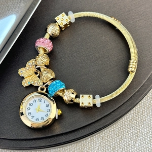 Close-up of golden beaded bracelet watch with butterfly pendant and white dial